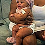 baby, child, smiling, pink_bonnet, fuzzy_slippers, diaper, arm, adult, couch, indoor, skin, happy, person, clothing, jewelry, holding, seated, closeup, family, love