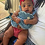 baby, child, person, headband, red_bow, denim_dress, outdoor, bench, lap, hand, car_key, curious_expression, skin, legs, clothing, casual, summer, sunlight, portrait, closeup