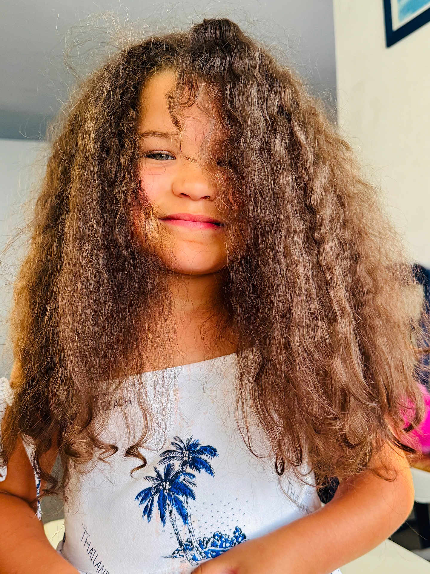 Victoire a rejoint le concours — aidez-le/la à gagner de superbes lots ! child, girl, smile, curly_hair, portrait, indoor, white_top, blue_print, palm_tree, casual_clothing, happy, young, person, face, hair, standing, closeup, natural_light, skin, candid