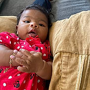 Thalia joined the competition — help win amazing prizes! adult_hand, baby, brown_eyes, child, close_up, couch, cozy, dark_hair, family, indoors, infant, lying_down, photography, pillow, polka_dots, portrait, red_dress, sitting, smiling, sofa
