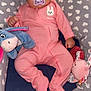 baby, sleeping, onesie, pink_clothing, pacifier, plush_toy, blue_donkey, pink_bunny_toy, cushion, heart_pattern, infant, child, cozy, indoor, cute, peaceful, soft_toys, resting, portrait, closeup