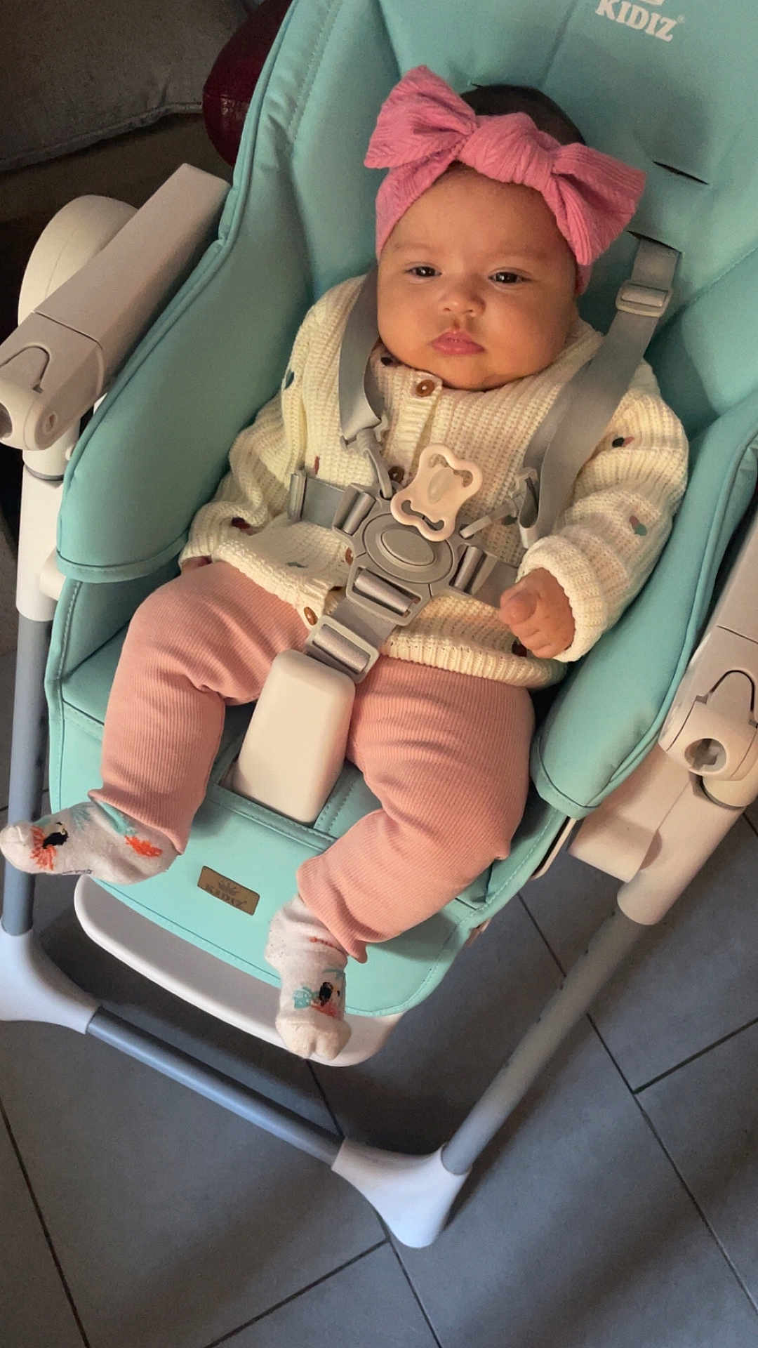 Rym participe au concours pour gagner de l'argent avec cette photo : baby, baby_accessory, baby_chair, baby_clothing, baby_furniture, baby_seat, child, cute, floor_tiles, headband, indoor, infant, knit_sweater, person, pink_bow, pink_pants, portrait, seatbelt, serious_expression, socks