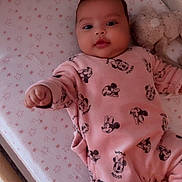 Rym participe au concours pour gagner de l'argent avec cette photo : baby, infant, pink_clothing, mickey_mouse, onesie, crib, mattress, star_pattern, plush_toy, bunny, cute, child, smiling, indoor, sleepwear, person, resting, young, soft_toy, cozy