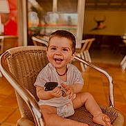 Ezio participe au concours pour gagner de l'argent avec cette photo : toddler, child, smiling, happy, sitting, chair, indoor, car_key, diaper, casual_clothing, woven_chair, barefoot, cute, portrait, baby, young_child, playful, joyful, person, expression