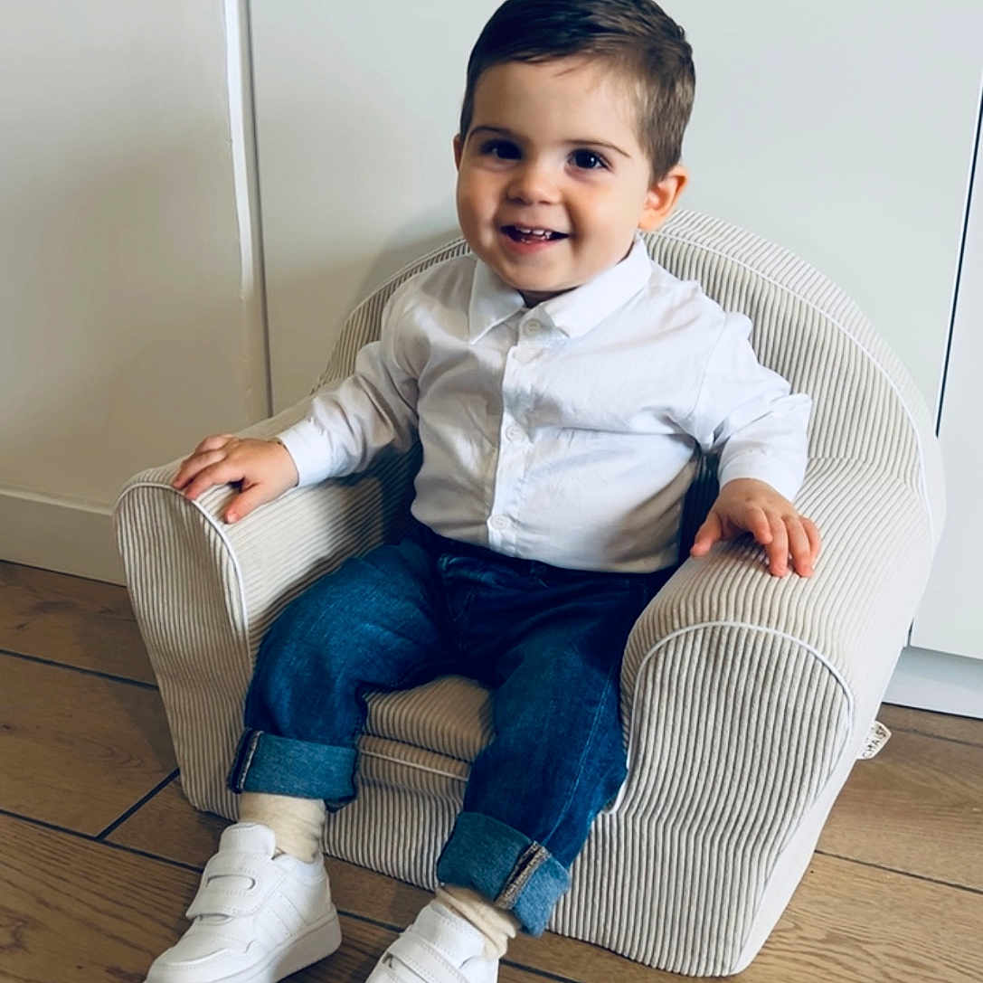 Ezio participe au concours pour gagner de l'argent avec cette photo : armchair, casual, child, cute, furniture, happy, home, indoor, jeans, person, portrait, seated, small_chair, smiling, sneakers, striped, toddler, white_shirt, wooden_floor, young_child