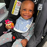 Camari joined the competition — help win amazing prizes! baby, child, car_seat, smiling, toy, bib, pajamas, seatbelt, infant, happy, indoors, vehicle_interior, black, holding, cute, face, person, safety, young_child, playful