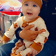 Maylon participe au concours pour gagner de l'argent avec cette photo : baby, child, infant, person, adult, clothing, onesie, hat, bear_pattern, indoor, sitting, lap, smiling, happy, jeans, jacket, blanket, furniture, background, cozy