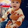baby, child, infant, person, adult, clothing, onesie, hat, bear_pattern, indoor, sitting, lap, smiling, happy, jeans, jacket, blanket, furniture, background, cozy