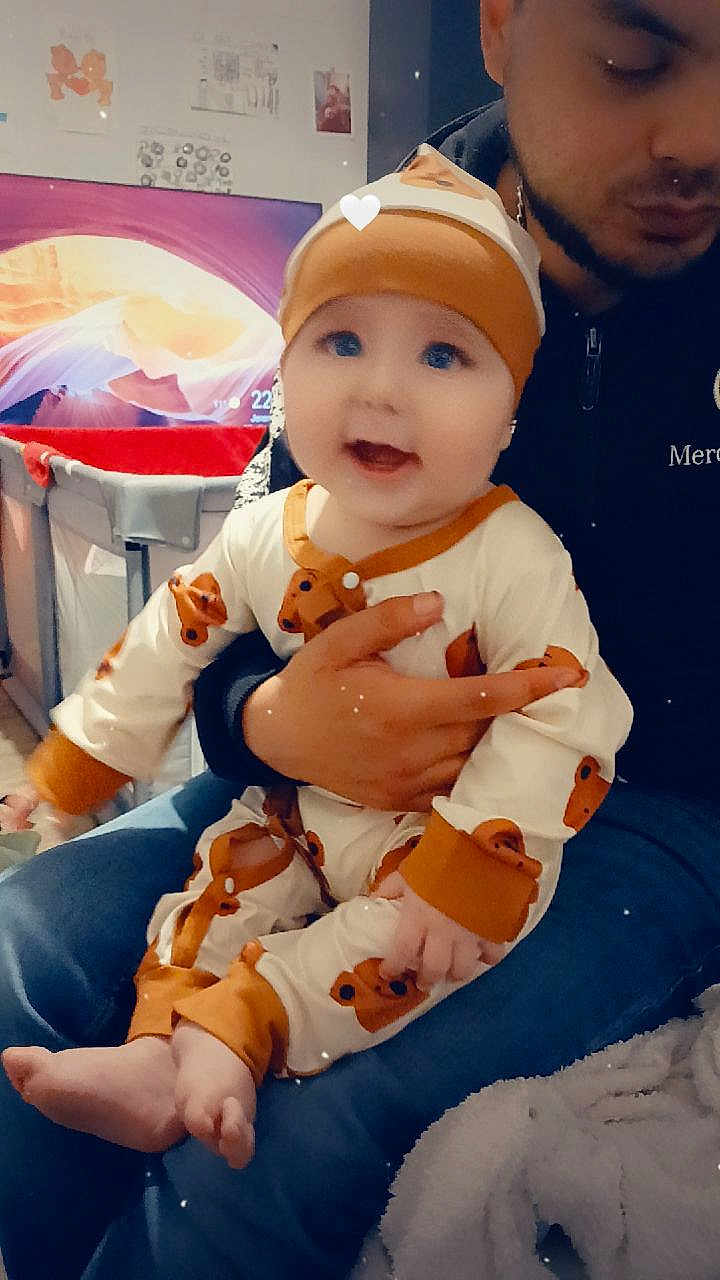 Maylon participe au concours pour gagner de l'argent avec cette photo : baby, child, infant, person, adult, clothing, onesie, hat, bear_pattern, indoor, sitting, lap, smiling, happy, jeans, jacket, blanket, furniture, background, cozy