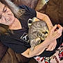 elderly_woman, cat, kitten, gray_tabby, couch, blanket, holiday_theme, candy_cane_pattern, resting, cozy, indoor, casual_clothing, black_shirt, wrinkled_skin, long_hair, sleeping_cat, holding, affection, relaxation, home