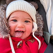 Charline a rejoint le concours — aidez-le/la à gagner de superbes lots ! baby, child, face, smile, tongue, hat, winter_clothing, red_jacket, fur_trim, cute, happy, closeup, portrait, cozy, playful, outdoor, infant, seatbelt, car_seat, childhood