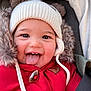 baby, child, face, smile, tongue, hat, winter_clothing, red_jacket, fur_trim, cute, happy, closeup, portrait, cozy, playful, outdoor, infant, seatbelt, car_seat, childhood