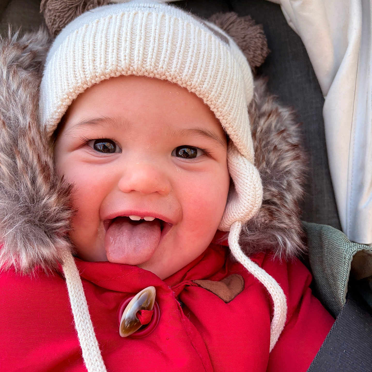 Charline a rejoint le concours — aidez-le/la à gagner de superbes lots ! baby, car_seat, child, childhood, closeup, cozy, cute, face, fur_trim, happy, hat, infant, outdoor, playful, portrait, red_jacket, seatbelt, smile, tongue, winter_clothing