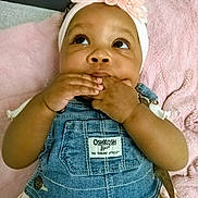 Karmen is registered to the contest to win money with this photo: baby, infant, denim_overalls, headband, flower_headband, pink_blanket, cute, hands, chewing, looking_up, child, clothing, soft_texture, indoors, portrait, young_child, person, skin, face, baby_girl
