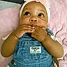 baby, infant, denim_overalls, headband, flower_headband, pink_blanket, cute, hands, chewing, looking_up, child, clothing, soft_texture, indoors, portrait, young_child, person, skin, face, baby_girl