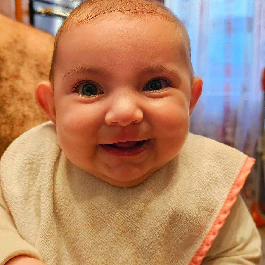Maïlana participe au concours pour gagner de l'argent avec cette photo : baby, bib, child, closeup, clothing, curtain, cute, face, hands, happy, indoor, infant, kitchen, person, portrait, sitting, skin, smiling, window, young_child
