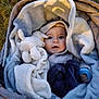 baby, blanket, plush_toy, stroller, outdoor, soft_texture, child, cute, warm, wrapped, face, blue_clothing, comfort, expression, toy, infant, cozy, person, nest, curious