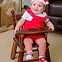 baby, child, smile, red_overalls, santa_hat, wooden_chair, indoors, happy, festive, holiday, cute, socks, furniture, person, portrait, seated, young_child, infant, warm_lighting, cozy