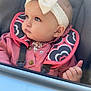 Miah is registered to the contest to win money with this photo: baby, child, headband, bow, car_seat, seatbelt, pink_jacket, face, portrait, infant, cute, looking_away, clothing, sitting, person, young_child, soft_light, indoors, closeup, baby_girl
