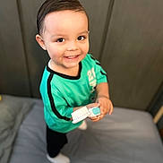 Kobe joined the competition — help win amazing prizes! toddler, child, smiling, toothbrush, bed, blanket, plush_toy, hair, green_shirt, black_pants, white_socks, indoor, person, happy, cute, portrait, room, soft_toys, furniture, playful