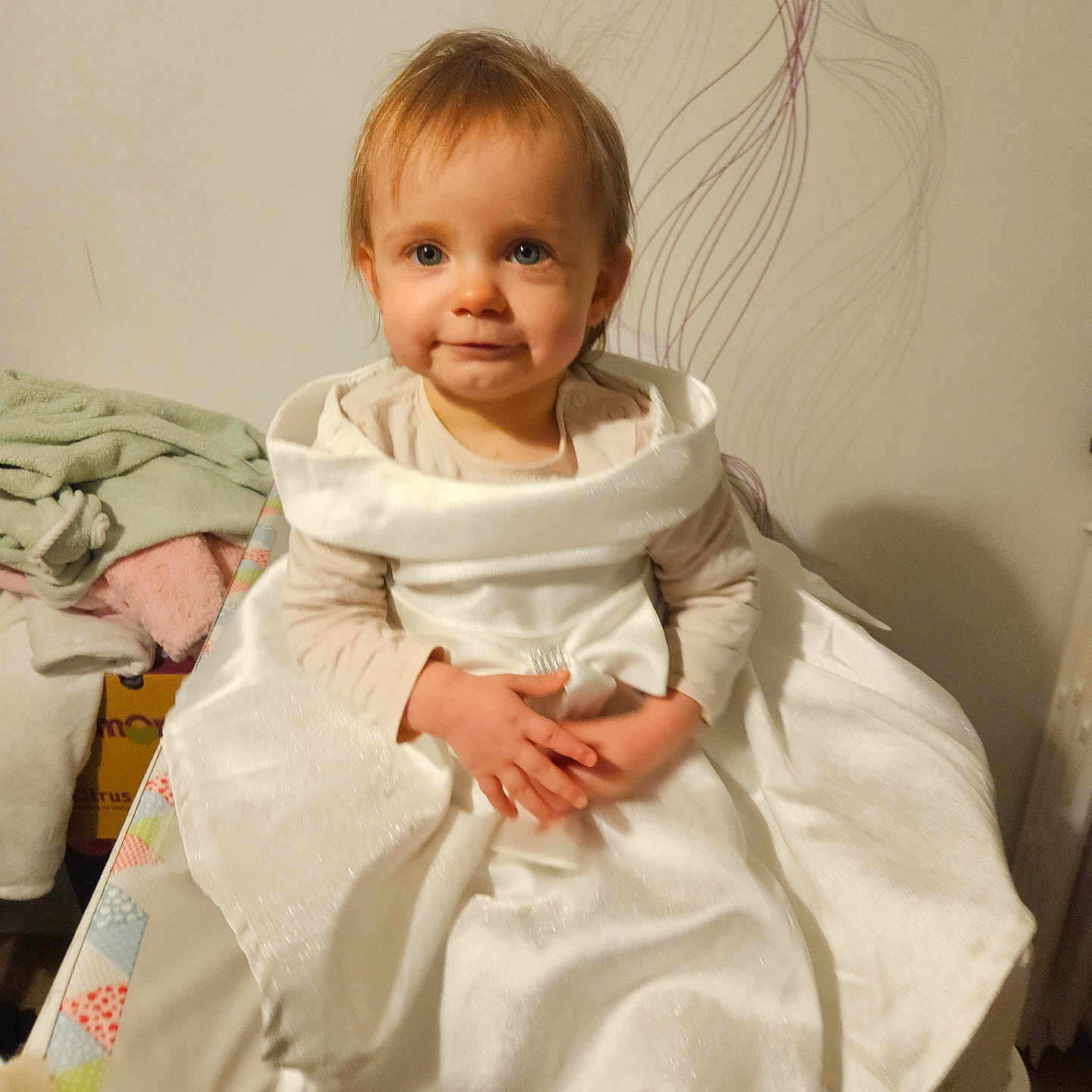 Louanna participe au concours pour gagner de l'argent avec cette photo : baby, child, clothing, cushion, cute, decor, fabric, floor, furniture, hands, home, indoor, person, portrait, sitting, smile, toddler, towel, wall, white_dress