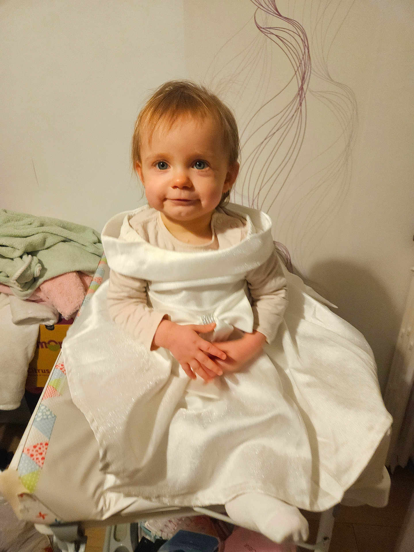 Louanna participe au concours pour gagner de l'argent avec cette photo : baby, child, clothing, cushion, cute, decor, fabric, floor, furniture, hands, home, indoor, person, portrait, sitting, smile, toddler, towel, wall, white_dress