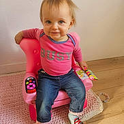 Louanna participe au concours pour gagner de l'argent avec cette photo : casual_clothing, child, colorful, cute, happy, indoor, jeans, knit_rug, person, pink_chair, pink_shirt, playful, seated, smiling, socks, toddler, toy, toy_book, wooden_floor, young_child