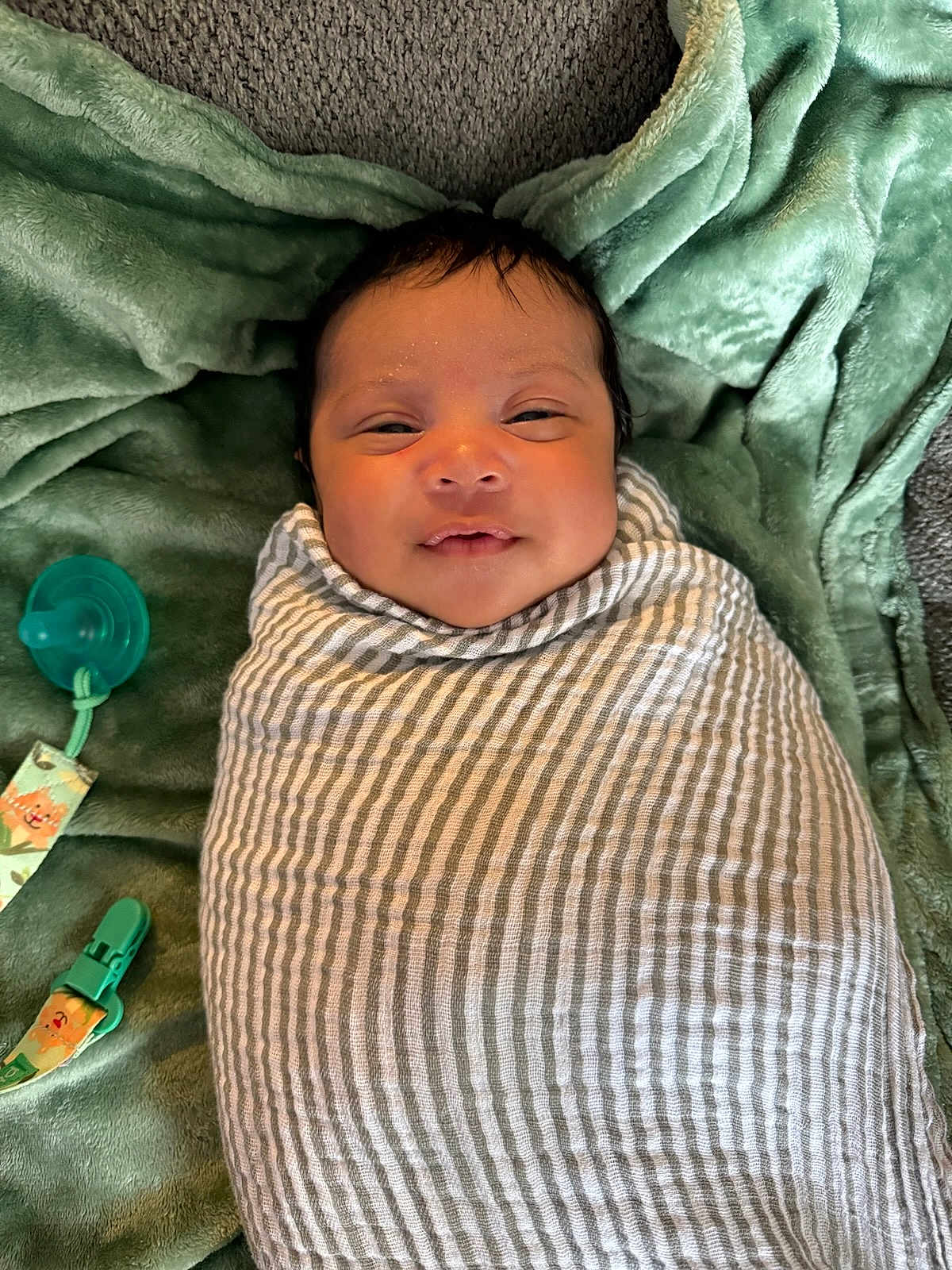 Maaer joined the competition — help win amazing prizes! baby, swaddle, blanket, pacifier, clip, infant, smile, face, lying_down, green_blanket, striped_cloth, newborn, cute, child, soft_texture, indoors, closeup, head, resting, comfort