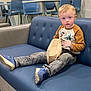 blonde_hair, blue_couch, blue_eyes, boy, casual, chairs, child, clothing, couch, curious, furniture, indoor, jeans, long_sleeve_shirt, paper_bag, portrait, shoes, sitting, table, young