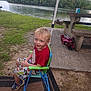 child, boy, smiling, chair, outdoor, lake, grass, trees, picnic_table, concrete, casual_clothing, shorts, sneakers, nature, water, daylight, recreation, relaxation, summer, vacation