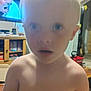child, blurry, indoor, shirtless, living_room, hair_tuft, face, expression, young, person, furniture, television, cabinet, toy, room, curious, portrait, home, casual, daylight