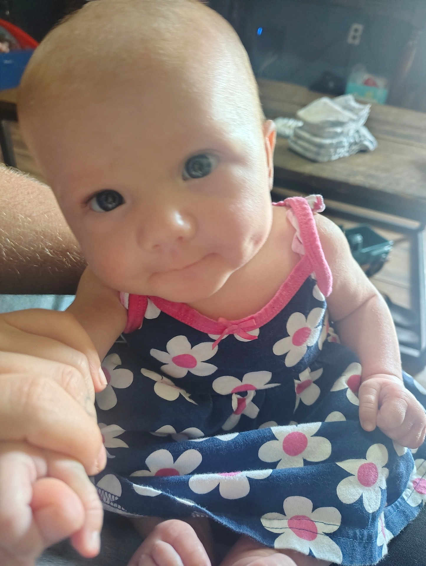 Delilah Rose Knight joined the competition — help win amazing prizes! baby, child, infant, person, dress, flower_pattern, hand, skin, face, eyes, indoor, furniture, table, clothing, cute, holding, closeup, pink, blue, smile