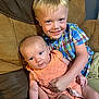 baby, boy, child, couch, smile, indoor, portrait, sitting, clothing, holding, person, infant, cute, family, happy, skin, face, furniture, blue_eyes, plaid_shirt