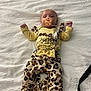 baby, baby_girl, bed, bow, child, clothing, cute, indoor, infant, infant_girl, leopard_print, lying_down, newborn, pacifier, patterned_pants, person, sleepwear, soft_texture, white_bedspread, yellow_clothing