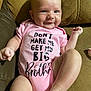 baby, brown_couch, child, couch, cute, face, feet, hand, happy, indoor, infant, legs, person, pink_onesie, portrait, sitting, skin, smiling, text_on_clothing, young_child