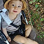 toddler, child, hat, stroller, outdoor, leaves, tree_bark, striped_shirt, shorts, footwear, happy, curious, baby, nature, seat_belt, playful, summer, smiling, person, portrait