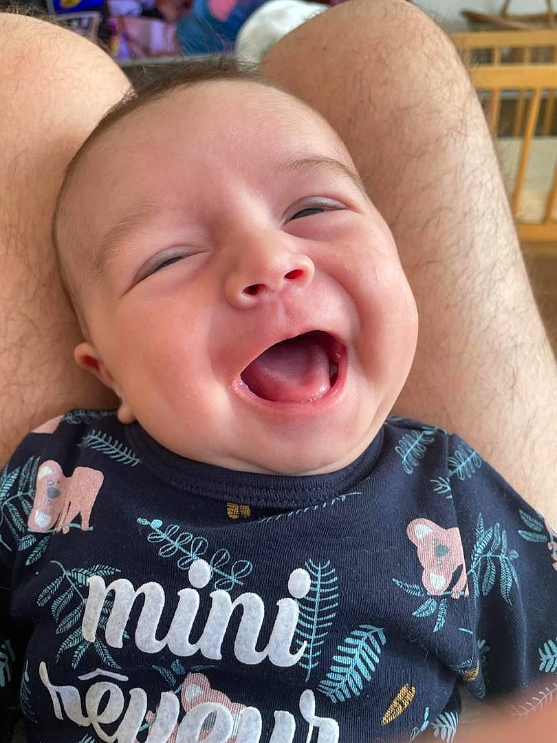 Hélios participe au concours pour gagner de l'argent avec cette photo : baby, baby_toddler_clothing, blue, cheek, chin, eyebrow, finger, gesture, happy, jaw, lip, mouth, nose, person, pink, skin, sleeve, smile, toddler, tongue