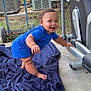 Kacey is registered to the contest to win money with this photo: baby, child, blue_clothing, blanket, outdoor, smiling, toy, bottle, exercise_equipment, grass, concrete, building, window, air_conditioner, handrail, person, standing, playful, happy, crawling