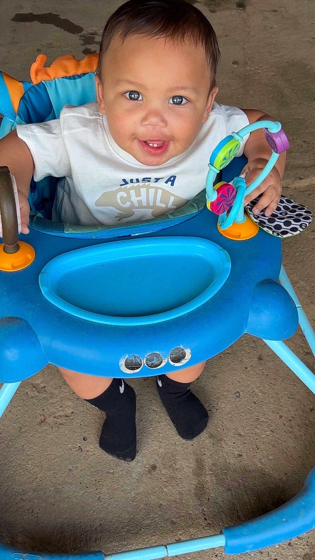 Kacey joined the competition — help win amazing prizes! baby, child, walker, toy, smiling, happy, white_shirt, black_socks, floor, concrete, blue, colorful, cute, infant, person, playtime, young_child, sitting, indoors, feet