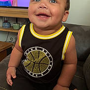 Kacey is registered to the contest to win money with this photo: toddler, child, smiling, sitting, couch, indoors, clothing, basketball, television, cartoon, person, happy, face, furniture, room, casual, cute, portrait, black_clothing, yellow_trim