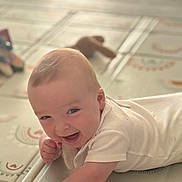élio a rejoint le concours — aidez-le/la à gagner de superbes lots ! baby, bright, cheerful, child, cute, face, floor, happy, indoor, infant, lying_down, patterned, play_mat, plush_toy, short_hair, skin, small_hand, smiling, white_clothing, young_child