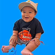 Martin joined the competition — help win amazing prizes! baby, child, cap, smiling, black_shirt, basketball_graphic, blue_toy, sitting, happy, cute, footwear_none, bracelets, shorts, indoor, portrait, playful, infant, bright_background, isolated, studio_style