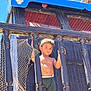 child, toddler, boy, shirtless, shorts, bracelet, necklace, wooden_railings, netting, pirate_ship, skull_decoration, blue_sky, outdoor, sunlight, daytime, portrait, serious_expression, standing, playground, adventure