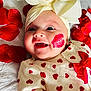 baby, bow, closeup, clothing, cute, face, happy, headband, heart_pattern, infant, infant_girl, lipstick_mark, lying_down, person, red_bow, red_hearts, rose_petals, skin, smiling, white_background