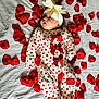Evie is registered to the contest to win money with this photo: adorable, baby, bow, child, clothing, cute, face, headband, heart_pattern, indoor, infant, lying_down, newborn, onesie, portrait, red_bows, rose_petals, soft_lighting, surprised_expression, white_sheet