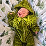 baby, infant, green_onesie, hooded_clothing, blanket, tree_pattern, sleepy_face, cute, cozy, soft_fabric, child, newborn, lying_down, hand, foot, zipped_jumpsuit, indoors, warm_clothing, smiling, relaxed