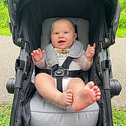 Jaxon is registered to the contest to win money with this photo: baby, baby_feet, blue_eyes, child, clothing, cute, footwear, grass, greenery, happy, infant, nature, outdoor, park, pavement, person, portrait, seatbelt, smiling, stroller