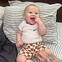 Jaxon joined the competition — help win amazing prizes! baby, bedroom, checkered_shorts, child, clothing, cute, hand, happy, human, indoor, infant, person, playful, portrait, sitting, smiling, striped_bed, striped_pillow, tattoo, white_onesie