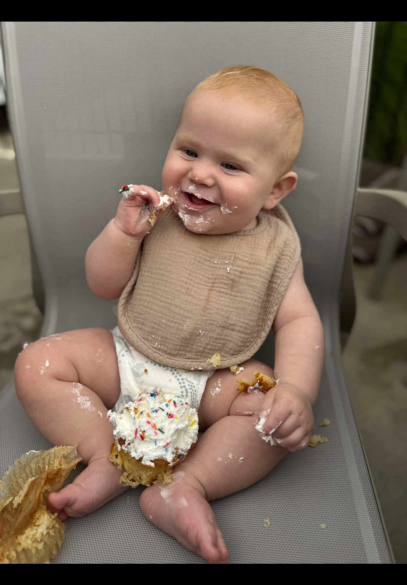 Jaxon is registered to the contest to win money with this photo: baby, child, cupcake, frosting, sprinkles, messy, smiling, sitting, bib, diaper, happy, food, chair, indoor, cute, chubby, hands, legs, face, celebration