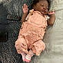 baby, sleeping, infant, pink_outfit, bow, bed, blanket, remote_control, smartphone, striped_socks, cute, peaceful, indoor, child, person, relaxing, soft_lighting, portrait, cozy, resting